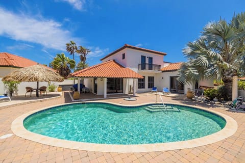 Exterior view of a Mediterranean-style vacation villa featuring terracotta roofing, white stucco walls, and palm tree landscaping with a private pool area.