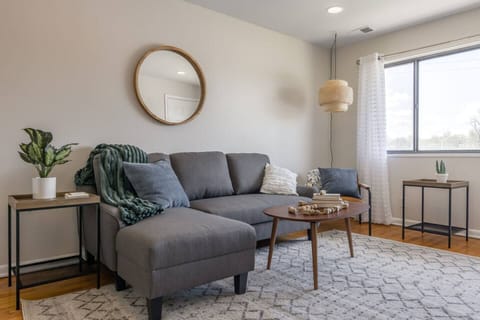 Bright, stylish living room with a plush sectional, modern decor, and soft natural light. Cozy textures, a statement mirror, and warm accents create the perfect space to relax, read, or unwind after a long day.