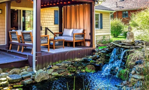 Covered patio lounge beside the waterfall and koi pond — your peaceful outdoor home base 