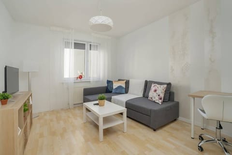 A bright living room with a grey sofa, a white coffee table, and wooden flooring.
