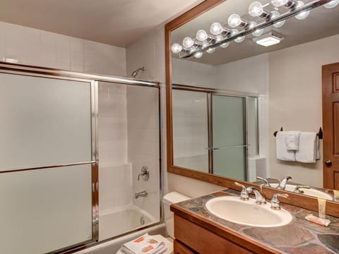 Bathroom featuring a combination bathtub and shower with frosted sliding glass doors, a large mirror above a sink, a wooden vanity, and white towels hanging on the wall.