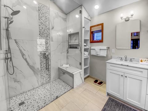 Indulge in the primary ensuite bathroom, a spa-like retreat featuring a spacious walk-in shower with a built-in bench, dual vanity sinks, and ample storage for a luxurious and comfortable stay.