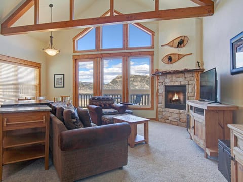 Nisa Mountain 36 - a SkyRun RMNP Property - Nisa Mountain 36 - Condo's main living area boasts floor to ceiling windows with stunning mountain views, a stone fireplace, flat screen TV, and ample seating from either the double sofa or loveseat. Opens up to the dining/kitchen area.