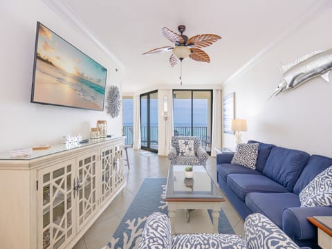 Cozy living area features a navy sofa with queen sleeper, elegant decor, and a view of the balcony overlooking the beach