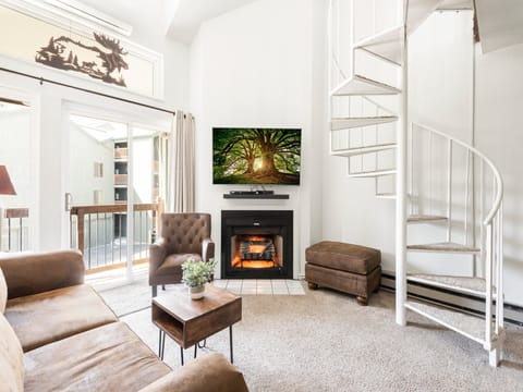 Bright living room with wall mounted flat screen TV and sound bar, spiral staircase leading to the loft