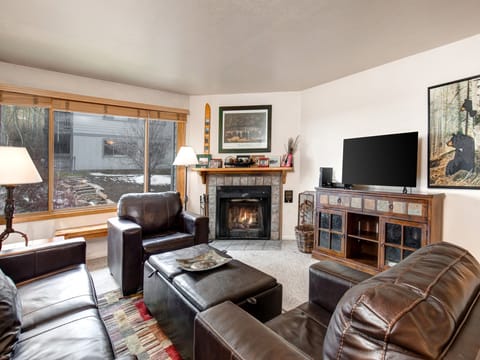 Snow Flower 65's living room with dark leather couch and club chair, coffee table, built-in fireplace and large window.