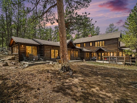 Rustic log cabin retreat nestled among towering pines, featuring warm glowing windows beneath a stunning twilight sky.