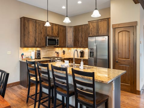 Bright, open kitchen with granite breakfast bar and seating for the whole group - Wood cabinetry and modern lighting add character to this welcoming space - Great for gathering around snacks, drinks, or morning pancakes