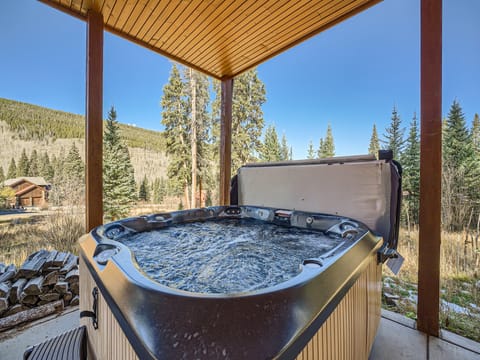 Outdoor hot tub on a wooden deck with a forest and mountain view in the background.