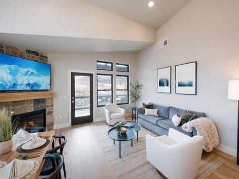 Relax in this bright, airy living room featuring soaring vaulted ceilings and a cozy stone fireplace. Large windows flood the space with natural light, while the open-concept design is perfect for family gatherings.