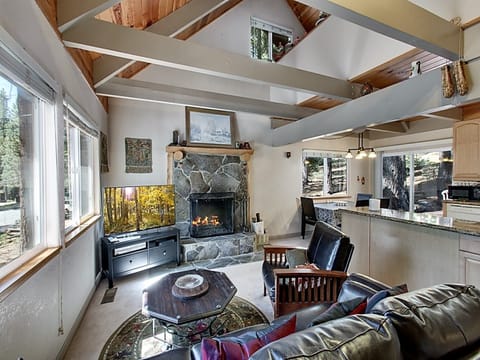 Cozy living room with vaulted ceilings, a stone fireplace, and large windows bringing in natural light.