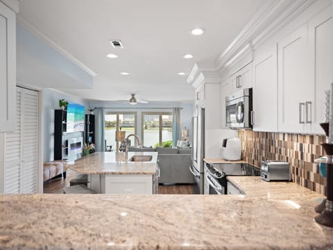 Open-concept kitchen and living area with granite countertops, stainless steel appliances, and custom tile backsplash. Bright and airy with lake views and coastal-inspired decor throughout.