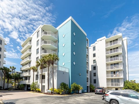 Modern beachside condominium complex featuring distinctive turquoise accent wall and tropical palm landscaping under bright Florida skies.
