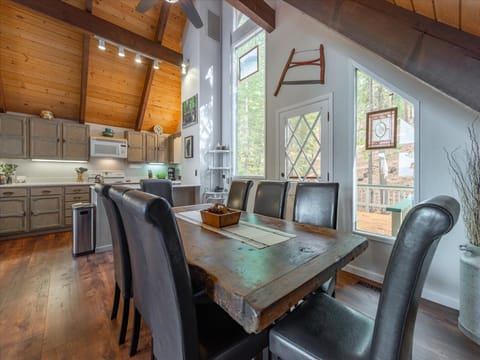Gather around this stunning rustic dining table beneath soaring wood beams and twinkling lights. The open kitchen flows seamlessly into your dining space, perfect for cooking together while enjoying forest views through large windows.