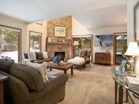Relax in this spacious living room featuring a stone fireplace, comfortable seating, and large windows that fill the space with natural light.