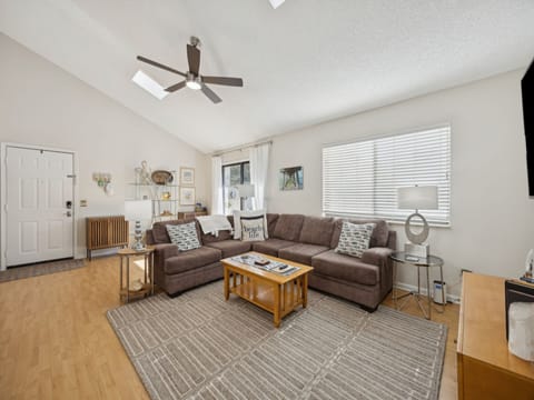 Relax in your comfortable living room with plush sectional seating, ceiling fan, and natural light streaming through large windows.
