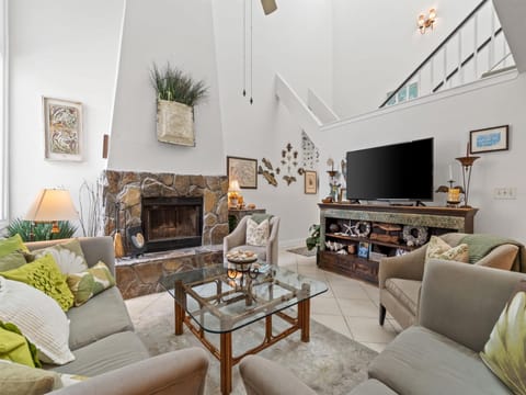 Unwind in your spacious living room where natural stone fireplace warmth meets modern comfort beneath soaring ceilings.