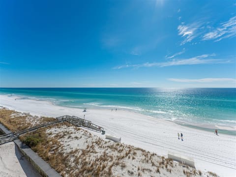 Pristine white sand beach with turquoise waters and wooden walkway access under brilliant blue skies.