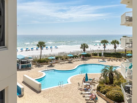 Oceanfront property overlooking a pristine beach and sparkling pool area with palm trees and sandy shores.