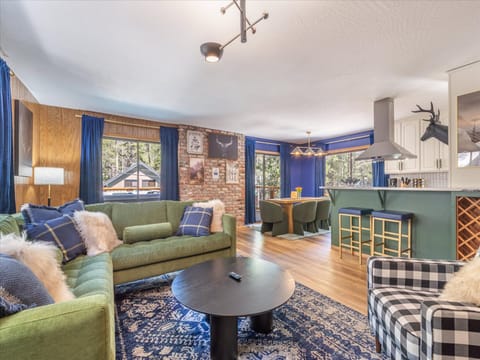 Unwind in your spacious living area featuring plush green sofas and a striking brick accent wall, perfectly connected to the modern kitchen.