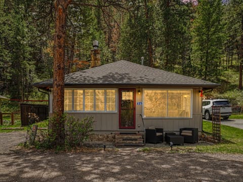 A charming cabin nestled among tall pines, offering a peaceful forest retreat with convenient parking and a cozy outdoor seating area at the entrance.