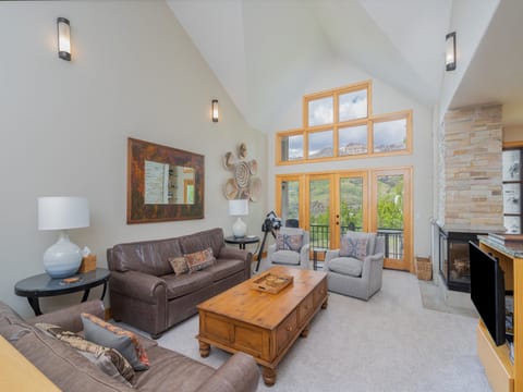 Your spacious living room invites relaxation with soaring vaulted ceilings, cozy seating, and stunning mountain views through expansive windows and balcony doors, perfect for unwinding after exploring.