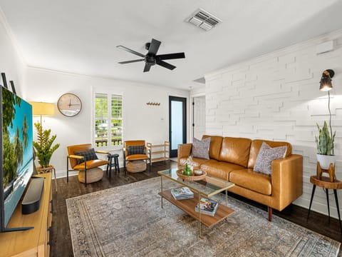 Sink into the buttery leather sofa and unwind in your stylish living room, where mid-century charm meets modern comfort beneath a cooling ceiling fan.
