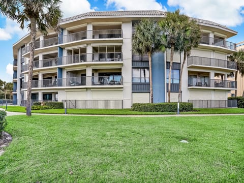 A modern multi-story property framed by swaying palm trees and manicured green lawns, offering a welcoming arrival experience beneath sunny skies.