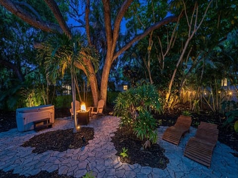 This tranquil evening retreat features a fire pit with seating, a private hot tub, and loungers nestled among lush tropical landscaping—perfect for unwinding under the stars.
