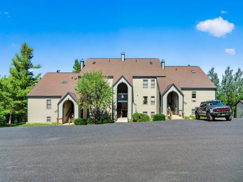The property features a multi-level building with arched entryways, set against a backdrop of lush greenery and clear blue skies, with convenient on-site parking for guests.