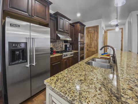 This gourmet chef's kitchen boasts a massive granite island with a double sink, premium stainless steel appliances, and rich dark cabinetry. It's the ultimate space for hosting and entertaining.
