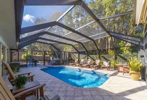 Screened pool area features a kidney-shaped pool, tiled deck, Adirondack chairs, and a hot tub in the back corner.