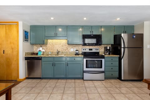 A kitchen with green cabinets, granite countertops, stainless steel appliances including a refrigerator, oven, microwave, and dishwasher. The floor is tiled.