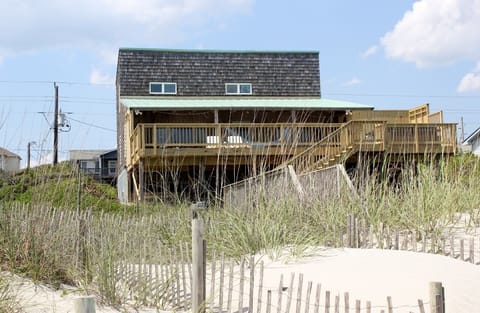 Charming oceanfront cottage with weathered shingles and expansive deck sits directly on pristine sandy dunes.