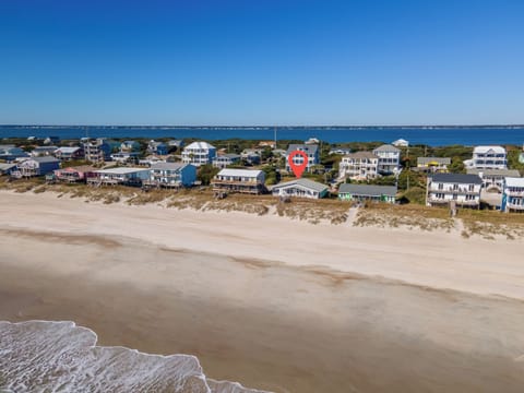 Aerial view of beachfront vacation homes along pristine sandy shores with crystal-clear waters stretching to the horizon.