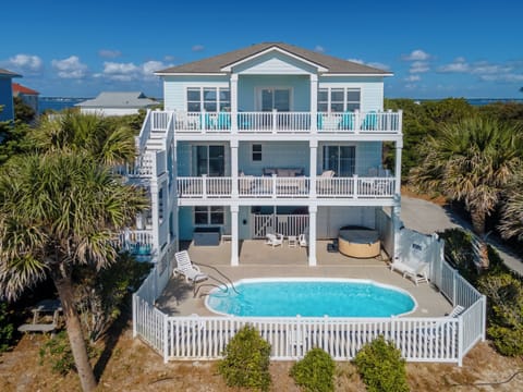 Stunning three-story beach house features private pool, hot tub, and multiple decks surrounded by tropical palms with ocean glimpses nearby.
