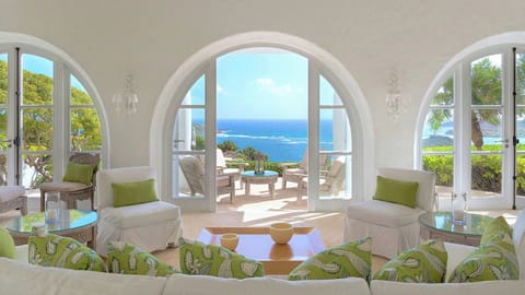 Large, high-ceilinged space well-appointed with comfortable off­-white sofas and armchairs with sage-green cushions. Wide, arched French doors open on three sides to let in sunlight and the ocean breeze. Opens onto the terrace, pool and ocean view on one 