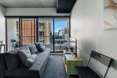 A modern living space with city views, featuring a cosy grey sofa, balcony access, and a functional setup perfect for relaxing and planning your day.

