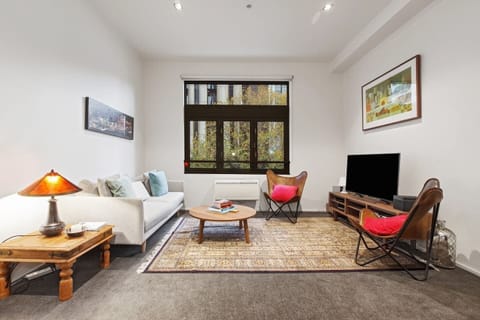 A funky living area has a two-person couch, additional leather armchairs, timber coffee table, modern wall art and a 40” Smart TV.