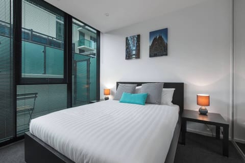 A modern and well-lit bedroom featuring a plush queen bed, built-in wardrobes with floor-to-ceiling mirrors and bedside tables