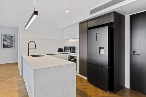 The sleek, open-plan kitchen is designed with stone countertops and high-quality Miele appliances, including an induction cooktop, oven, and dishwasher. 