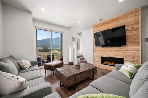 Experience the cozy living room, outfitted with plush seating, an expansive smart TV, and sliding patio doors that frame the breathtaking mountain vistas.