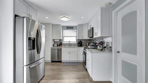 Immaculate white cupboards adorn the walls, complemented by the sleek sophistication of black and stainless finish appliances.