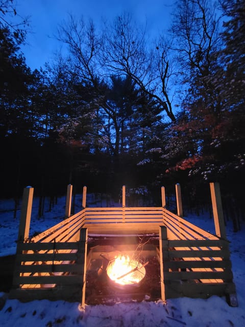 Cozy up by the fire under a winter-blue sky, with snow-dusted woods creating a peaceful, cabin-style escape.