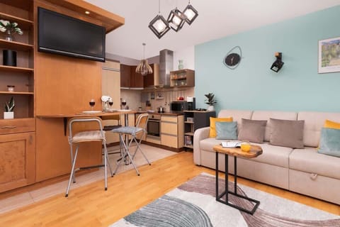 An open view of the living space with a wall-mounted TV, wooden cabinetry, and bar stools, providing a functional and stylish setup.

