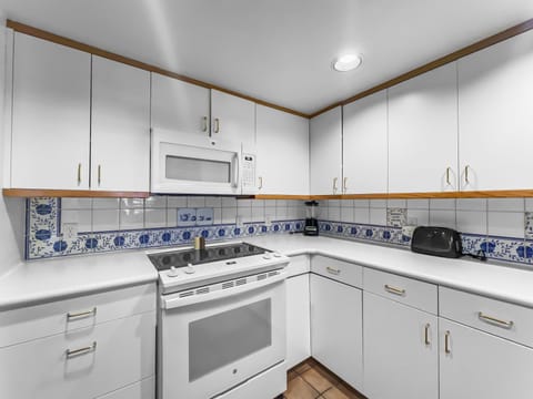 A white kitchen features white cabinets, a countertop with a toaster, a microwave above a stove, and a decorative blue and white tiled backsplash.
