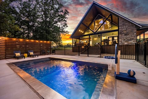 Modern backyard pool glows with sunset hues, and lights in Broken Bow, OK.