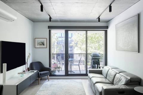 Relax in style in the sunlit living space, featuring a comfortable leather lounge and a large TV.