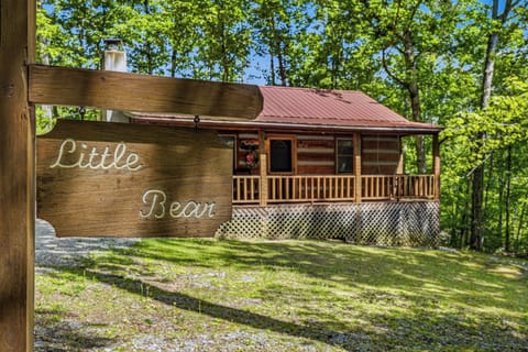 A charming log cabin named 'Little Bear' nestled among lush green trees, offering a peaceful retreat surrounded by nature.