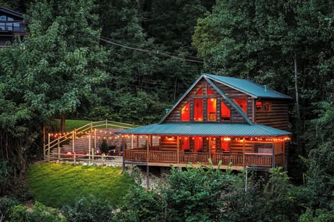 A secluded log cabin surrounded by towering trees in a lush forest setting, offering a peaceful mountain retreat with warm lighting and spacious decks for outdoor relaxation.